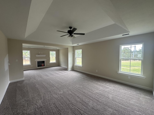 unfurnished living room featuring carpet, a raised ceiling, ceiling fan, and a healthy amount of sunlight