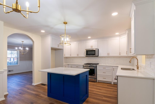 kitchen with arched walkways, dark wood finished floors, stainless steel appliances, a sink, and a chandelier