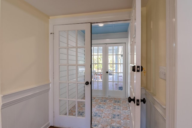 doorway featuring french doors, wainscoting, and a decorative wall