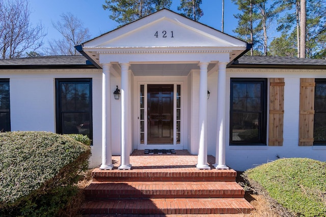 property entrance featuring a shingled roof and brick siding