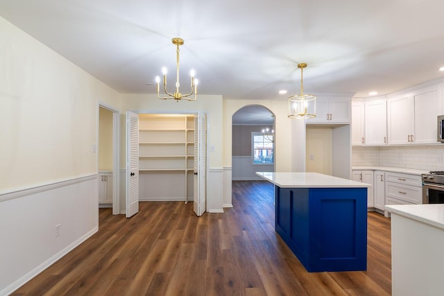 kitchen with arched walkways, white cabinets, light countertops, appliances with stainless steel finishes, and dark wood finished floors