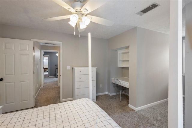 carpeted bedroom featuring a textured ceiling, ceiling fan, and built in desk