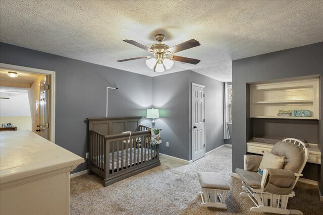 bedroom featuring a textured ceiling, light colored carpet, ceiling fan, a crib, and a closet