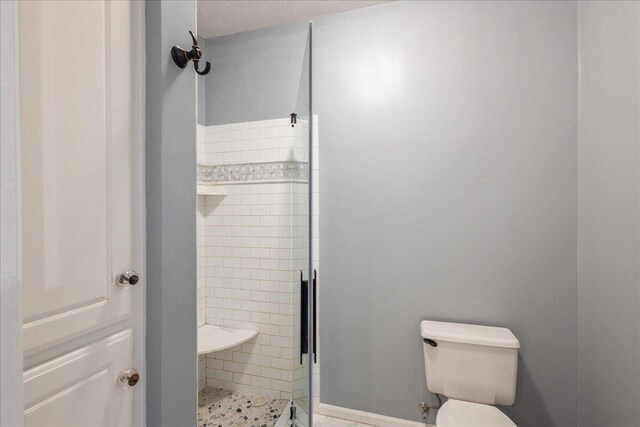 bathroom featuring toilet, a tile shower, and a textured ceiling