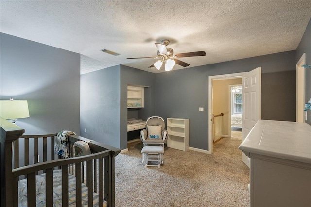 bedroom featuring light carpet, a textured ceiling, a nursery area, and ceiling fan