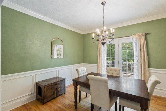 dining room with a notable chandelier, light hardwood / wood-style floors, ornamental molding, and a textured ceiling