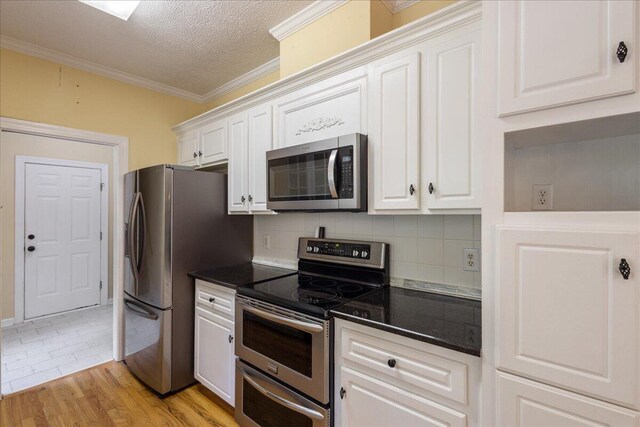 kitchen with decorative backsplash, white cabinets, light wood-type flooring, and appliances with stainless steel finishes