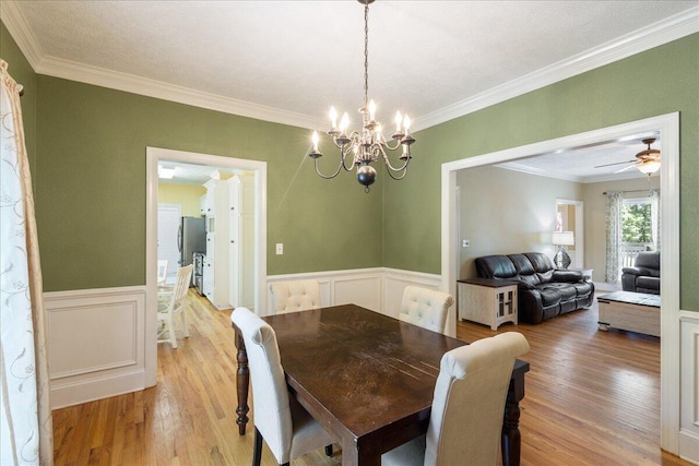 dining space featuring ceiling fan with notable chandelier, a textured ceiling, light wood-type flooring, and ornamental molding