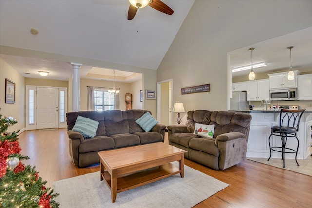 living room featuring a towering ceiling, ceiling fan with notable chandelier, light hardwood / wood-style flooring, and ornate columns