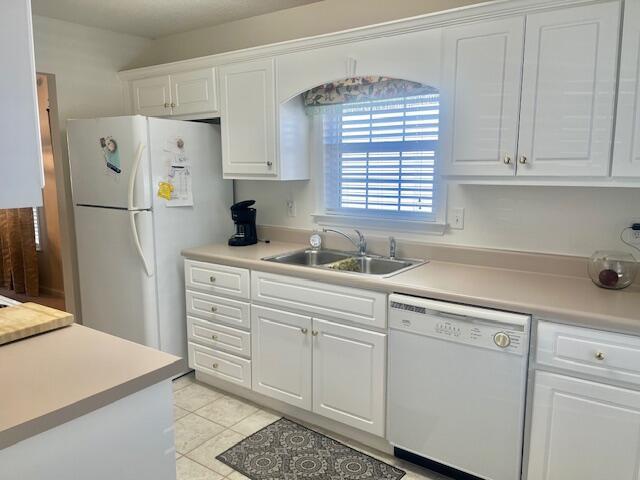 kitchen with light countertops, white appliances, a sink, and white cabinetry