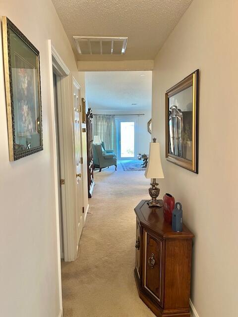 corridor featuring light carpet, a textured ceiling, visible vents, and baseboards