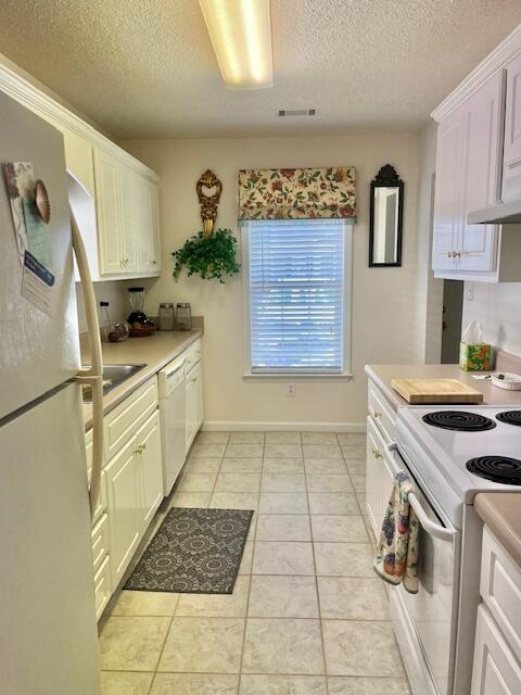 kitchen with light tile patterned floors, light countertops, visible vents, white cabinets, and white appliances