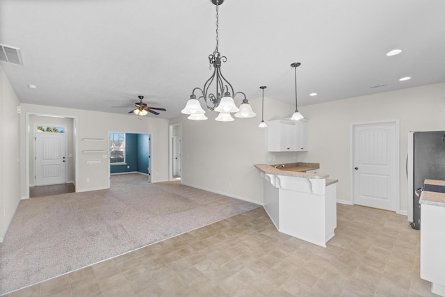 kitchen with light colored carpet, a peninsula, visible vents, white cabinetry, and freestanding refrigerator