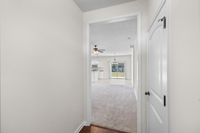 hallway with carpet flooring, a textured ceiling, baseboards, and wood finished floors