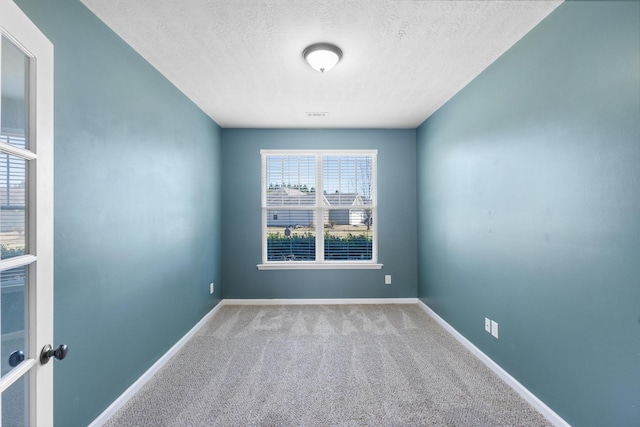 unfurnished room with a textured ceiling, carpet flooring, visible vents, and baseboards