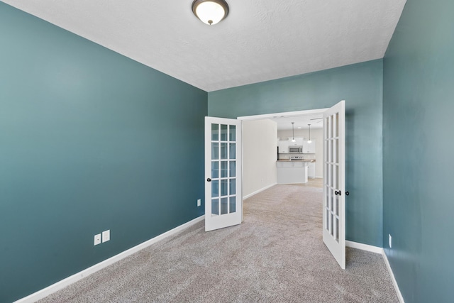 carpeted empty room featuring baseboards, a textured ceiling, and french doors