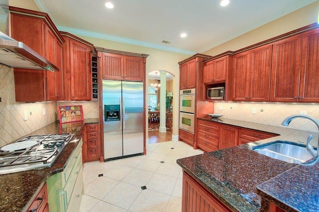 kitchen with a sink, arched walkways, appliances with stainless steel finishes, wall chimney exhaust hood, and decorative columns