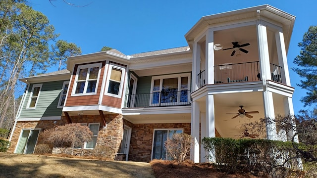 view of front of property featuring a balcony, a ceiling fan, and stone siding