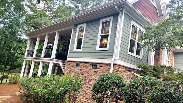 view of side of property with stone siding, a sunroom, and ceiling fan