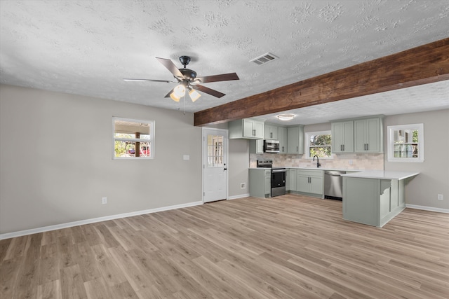 kitchen with backsplash, sink, light wood-type flooring, a textured ceiling, and appliances with stainless steel finishes