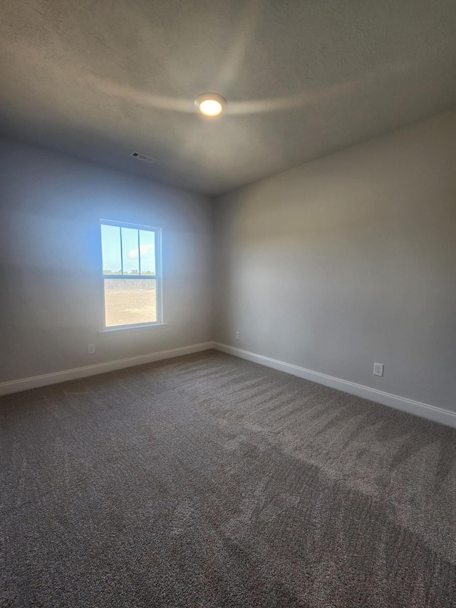 empty room featuring visible vents, baseboards, and dark carpet