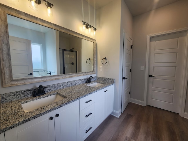 bathroom with double vanity, a sink, a shower stall, and wood finished floors