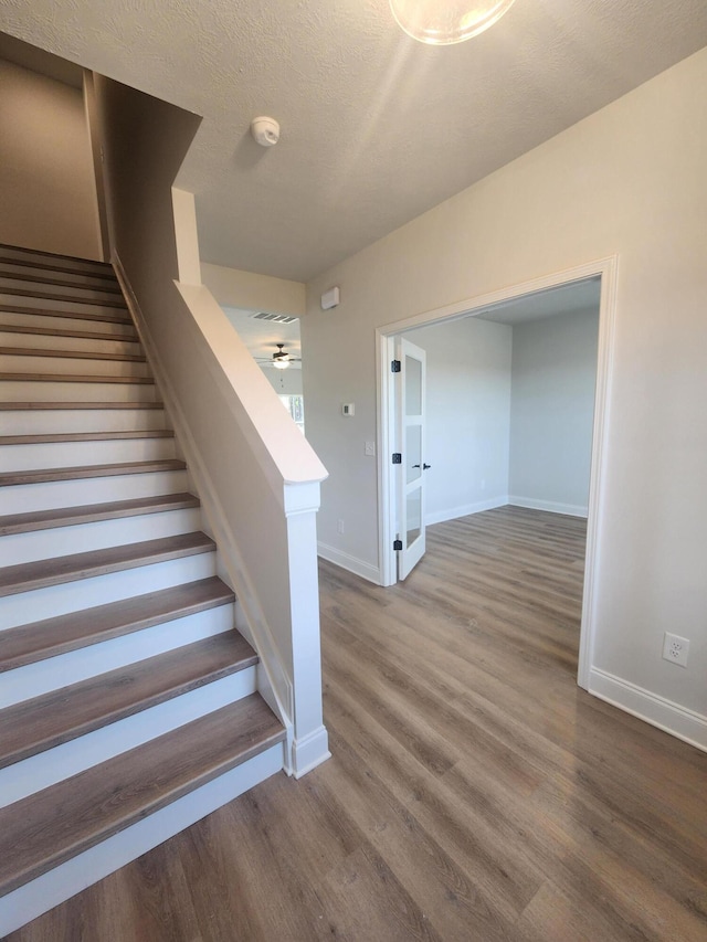 stairs with ceiling fan, a textured ceiling, baseboards, and wood finished floors