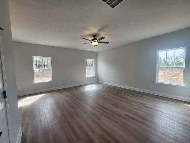 empty room featuring a ceiling fan, dark wood-style flooring, visible vents, and baseboards