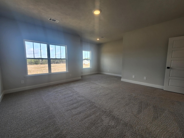 empty room with baseboards, visible vents, and dark carpet