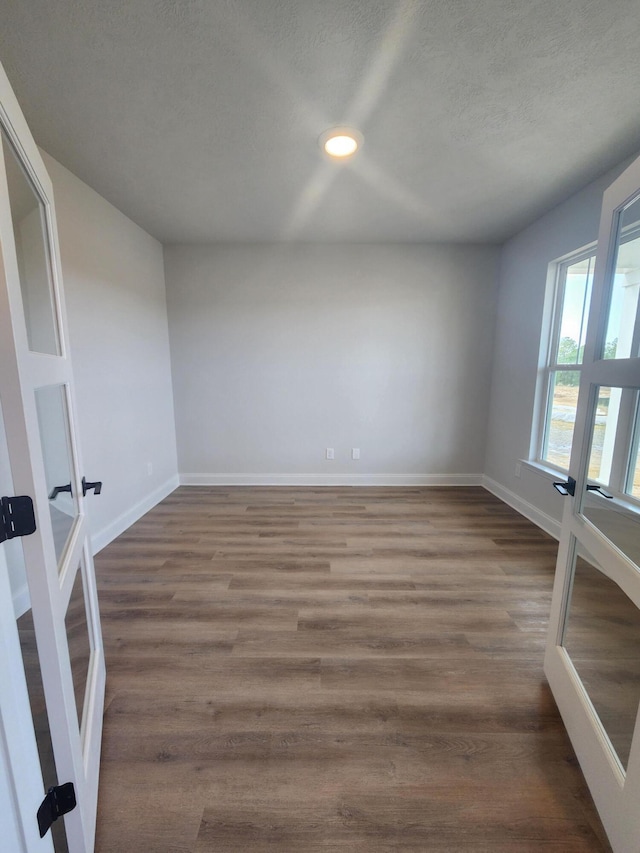 spare room featuring a textured ceiling, french doors, dark wood-style flooring, and baseboards