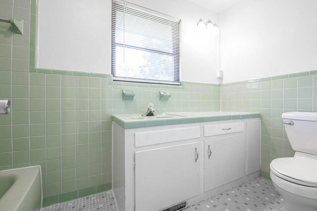 bathroom with vanity, toilet, tile walls, and a tub