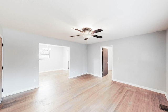 empty room featuring ceiling fan with notable chandelier and light wood-type flooring