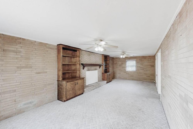 unfurnished living room with a brick fireplace, ornamental molding, brick wall, light colored carpet, and ceiling fan