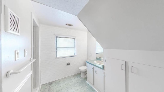 bathroom featuring a textured ceiling, vanity, toilet, and lofted ceiling