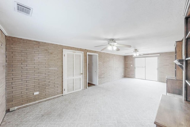 interior space featuring a textured ceiling, light colored carpet, ceiling fan, and brick wall