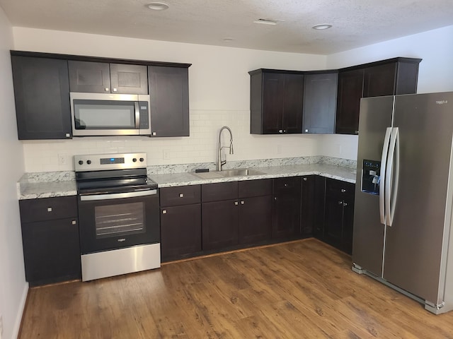 kitchen with sink, light stone counters, a textured ceiling, appliances with stainless steel finishes, and hardwood / wood-style flooring