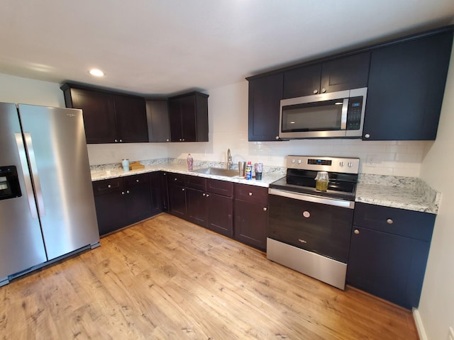 kitchen with light hardwood / wood-style floors, sink, light stone countertops, and stainless steel appliances