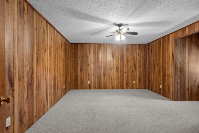 carpeted spare room featuring wood walls, ceiling fan, and a textured ceiling