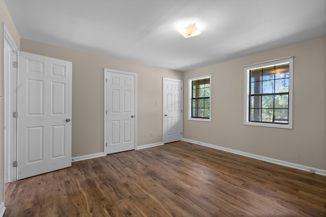 unfurnished bedroom with dark wood-type flooring and two closets