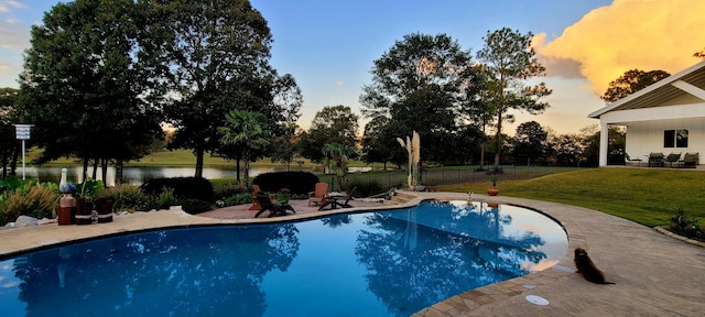 pool at dusk featuring a lawn, a patio area, and a water view