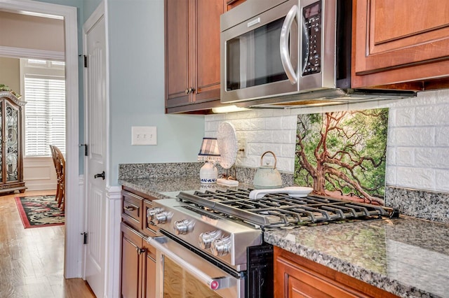 kitchen featuring decorative backsplash, stainless steel appliances, light stone counters, and light hardwood / wood-style flooring