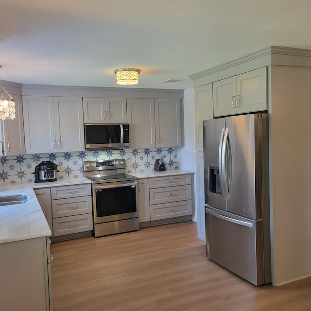 3597 Parliament Pl, Martinez, GA 30907 - kitchen featuring appliances with stainless steel finishes, backsplash, light wood-style floors, light stone countertops, and a chandelier
