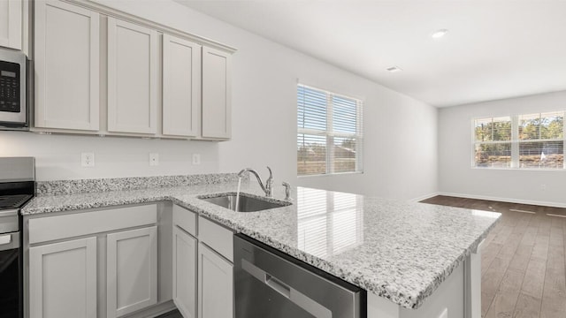 kitchen featuring stainless steel appliances, a sink, light stone counters, a peninsula, and wood finished floors