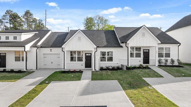 view of front of house featuring board and batten siding, driveway, a front yard, brick siding, and a garage