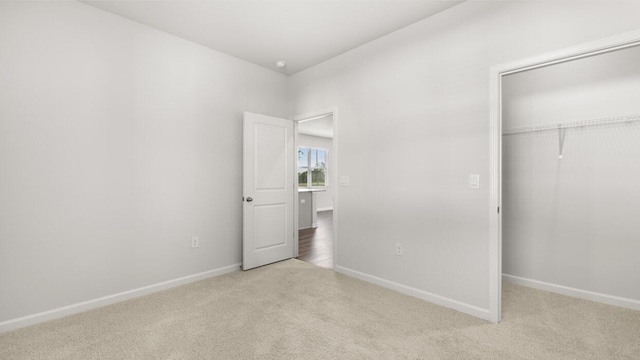 unfurnished bedroom featuring baseboards, a closet, and light colored carpet