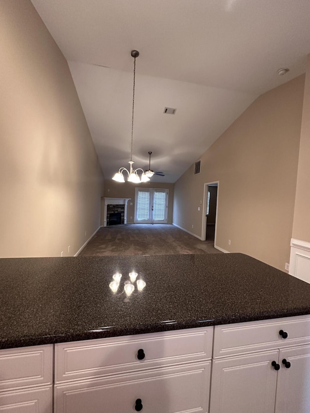 kitchen featuring lofted ceiling, a stone fireplace, white cabinetry, hanging light fixtures, and carpet flooring