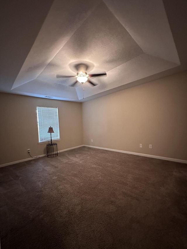 carpeted spare room with a raised ceiling and ceiling fan