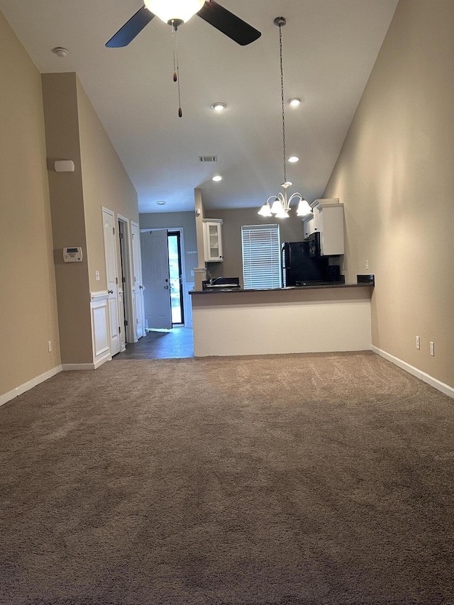 unfurnished living room featuring lofted ceiling, ceiling fan with notable chandelier, and dark colored carpet