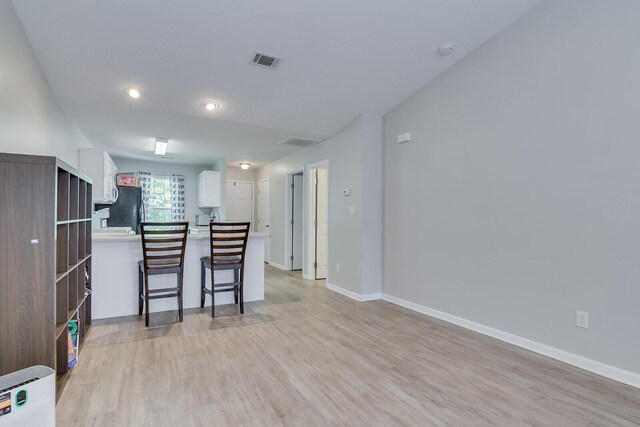 kitchen with a kitchen breakfast bar, white cabinetry, freestanding refrigerator, light wood-style floors, and visible vents