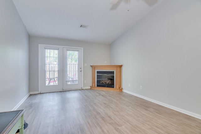 unfurnished living room with a glass covered fireplace, baseboards, a ceiling fan, visible vents, and wood finished floors
